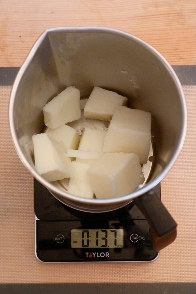 Blocks of white candle wax in metal pitcher on top of a digital scale.