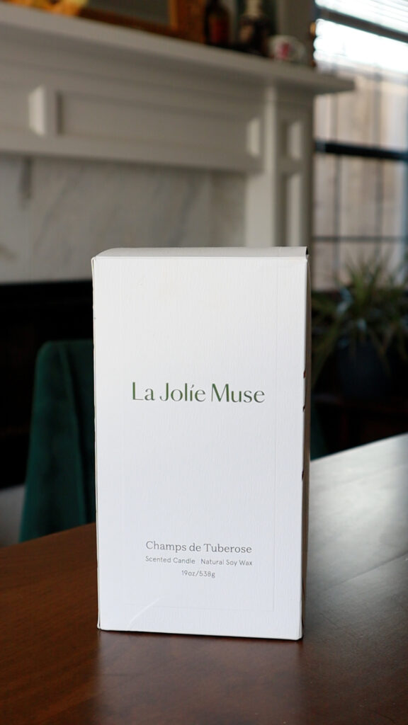 White cardboard box with La Jolie Muse Champs de Tuberose candle inside.