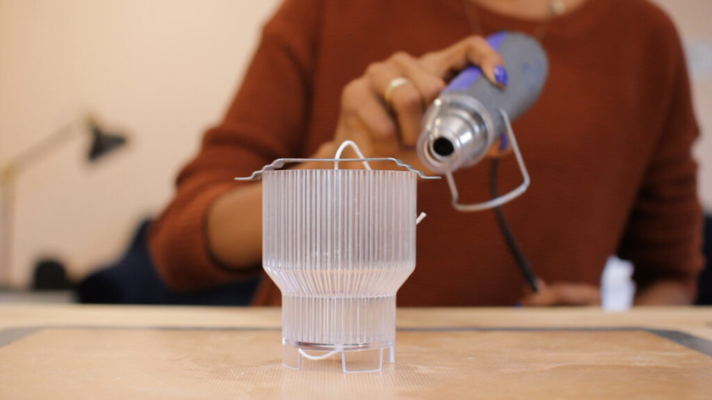 Hand holding a heat gun pointed toward an empty acrylic candle mold.