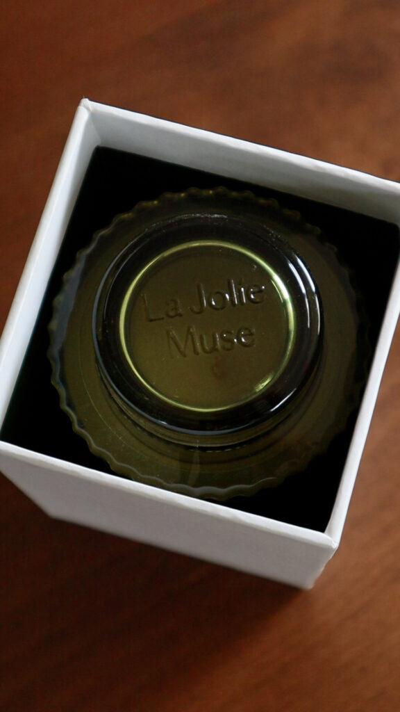 Overhead view of a green glass La Jolie Muse Mandarin Matcha candle jar inside of a white box.