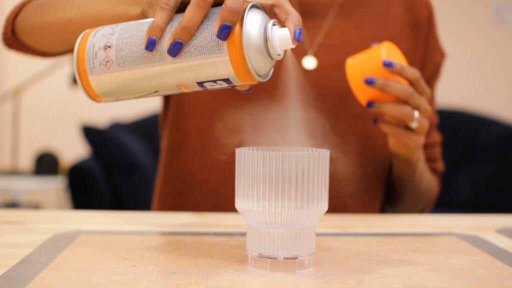 Hand spraying mold release spray into an empty acrylic candle mold.