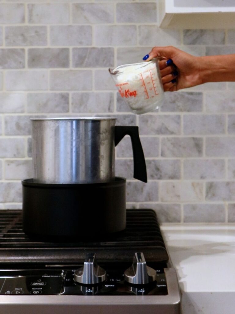Hand pouring candle wax into a double boiler.