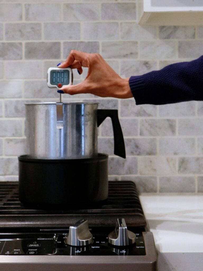 Clipping a thermometer to a double boiler that is set up to melt candle wax.