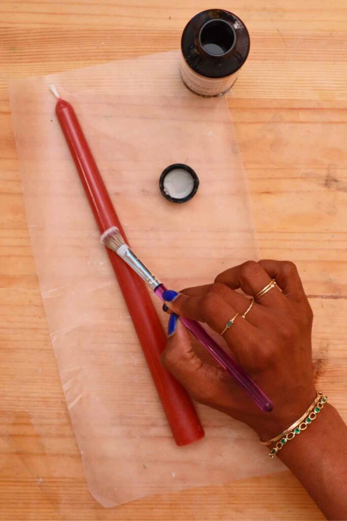 hand brushing candle gloss oto a red taper candle